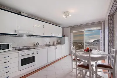 a kitchen with white cabinets and a table with chairs at Apartamento Varandas do Mar, Praia dos Pescadores, Albufeira in Albufeira