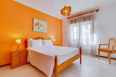 a bedroom with orange walls and a bed and a chair at Apartamento T1 praia in Quarteira