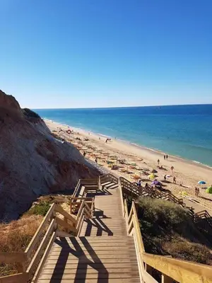 a wooden boardwalk leading to a beach with umbrellas at GelbBlau Falésia in Albufeira