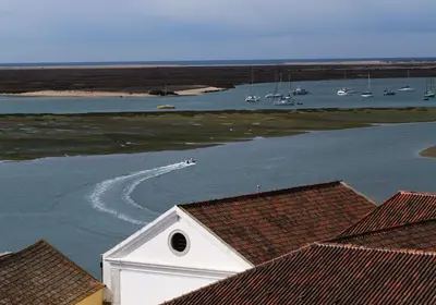 a boat traveling down a river with boats in the water at 1977 in Faro