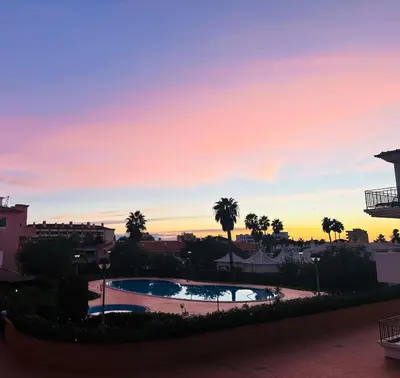 a sunset view of a swimming pool with palm trees at Appartement Villamoura in Vilamoura