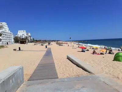 a beach with a wooden boardwalk and people on it at SATÉLITE AC&Garagem in Quarteira
