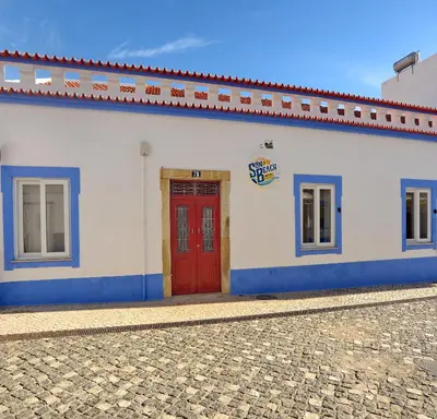 a white building with a red door on a street at Son of a Beach Hostel in Albufeira