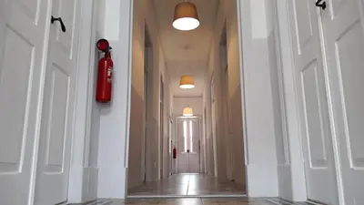 a hallway with white walls and a red fire extinguisher on the wall at Hostel A Casa da Árvore in Faro