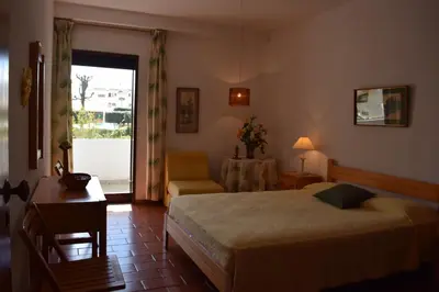a bedroom with a bed and a chair and a table at Apartamento T2 com Piscina e Wifi a 350 metros da Praia in Roja- Pé