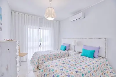 a white bedroom with two beds and a window at APARTAMENTO MICÁ in Albufeira