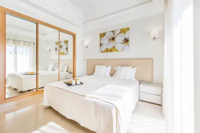 a white bedroom with a large bed and a mirror at Lakeside Country Club - Apartamentos Turísticos in Quinta do Lago