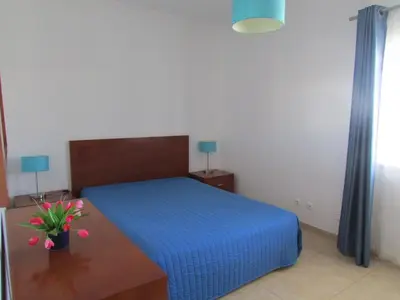 a bedroom with a blue bed and a table with flowers at Apartamentos Cabrita in Albufeira