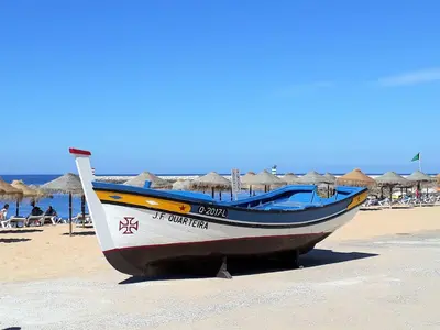 a boat sitting on a beach with umbrellas at Dunas 3- Elegante, 150mt Praia, Wifi in Quarteira