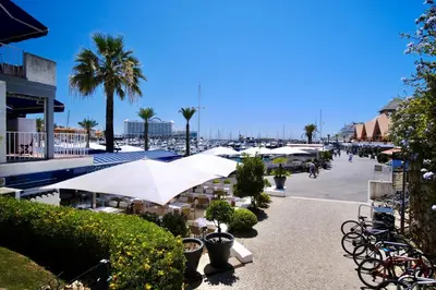 a street with tables and umbrellas and palm trees at Renovated Vilamoura Penthouse Near Marina & Beach in Vilamoura