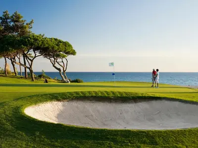 two people standing on a golf course with the ocean in the background at Ria Park Garden Hotel in Vale do Lobo
