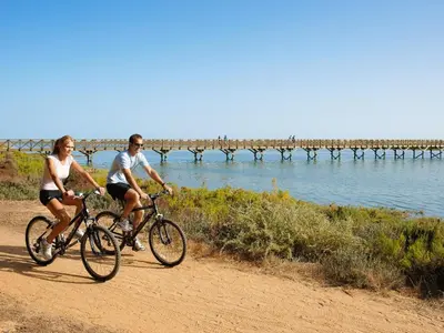 two people riding bikes on a dirt road near the water at Vale Do Garrao Villas in Vale do Lobo