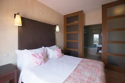 a bedroom with a bed with white sheets and pink pillows at Hotel Parque das Laranjeiras in Vilamoura