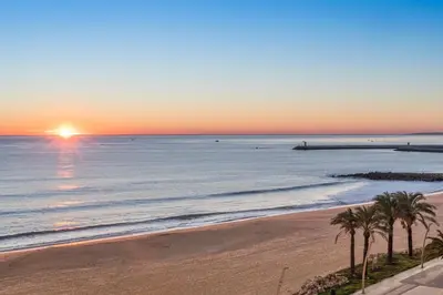 a sunset over the ocean with palm trees on a beach at Dom Jose Beach Hotel (Plus) in Quarteira