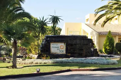 a sign in front of a building with palm trees at Hotel Pinhal do Sol in Quarteira