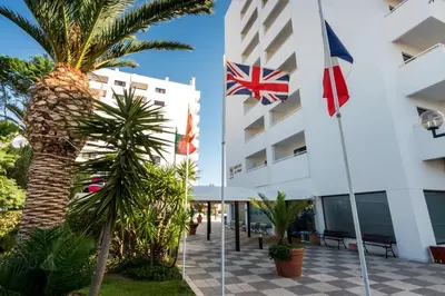a hotel with flags in front of a building at Janelas do Mar Apartamentos Turisticos in Albufeira