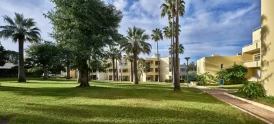 a park with palm trees in front of a building at Parque Mourabel, Oásis Village & Pé do Lago in Vilamoura