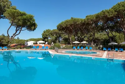a large swimming pool with blue chairs and umbrellas at Apartamentos Turisticos Pinhal Da Marina in Vilamoura
