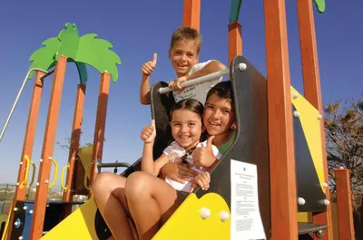 three children sitting on a slide at a playground at Hotel Apartamento Balaia Atlantico in Albufeira