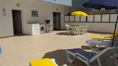 a living room with chairs and a table with a yellow umbrella at T2 Tahíti - Terraço, Familiar, Garagem, Wifi in Quarteira