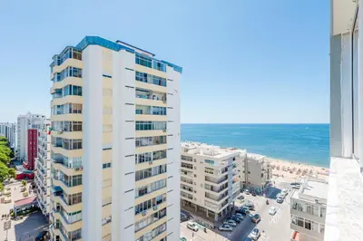 a tall white building with the ocean in the background at Vista Mar in Quarteira