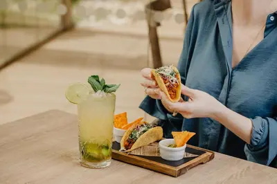a woman eating a sandwich and a drink on a table at Aqua Pedra Dos Bicos Design Beach Hotel - Adults Friendly in Albufeira