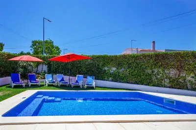 a swimming pool with chairs and umbrellas next to a hedge at LOTUS VILLA, Albufeira in Albufeira