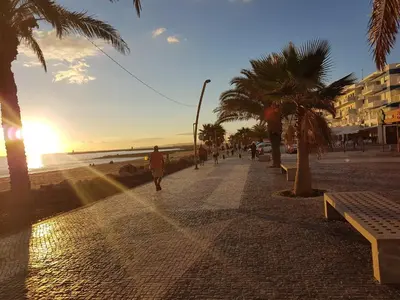 a person walking down a sidewalk next to the beach at Apartment Girasol Front Beach Quarteira Algarve in Quarteira