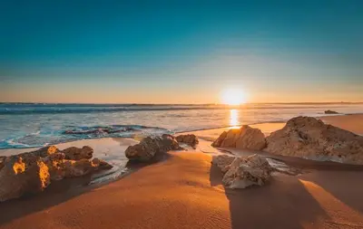 a sunset on a beach with rocks in the sand at Spacious apartment in Albufeira 80 m² with shared pool in Roja- Pé