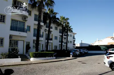 a building with palm trees and cars parked in a parking lot at Apartamento com Piscina em Albufeira, Praia da Oura in Albufeira