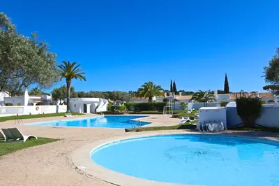 a swimming pool in a resort with palm trees and houses at Aldeia do Golf 151 - Clever Details in Vilamoura