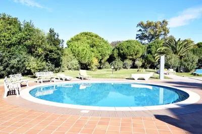 a swimming pool with chairs and a table and trees at Casa Flor in Vilamoura