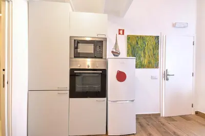 a white kitchen with a microwave and a refrigerator at Yellow Barqueta Studio in Faro