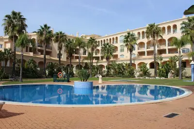 a pool in front of a building with palm trees at Los Arcos Apartment I in Vilamoura