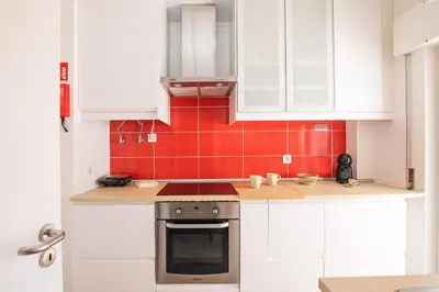 a kitchen with white cabinets and a red tiled wall at Beti Oura Village in Albufeira
