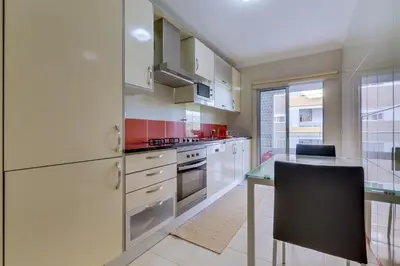 a kitchen with white cabinets and a table with chairs at Forte Novo - Modern apartment - Quarteira in Quarteira