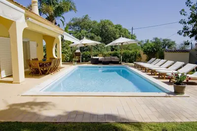 a swimming pool in a backyard with chairs and an umbrella at Villa Jasmim in Almancil