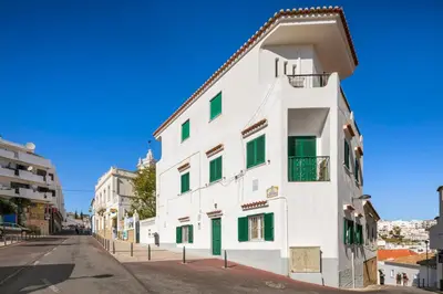 a white building with green shutters on a street at Casa da Vila in Albufeira