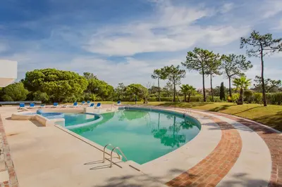 a large swimming pool in a park with trees at Victory Beach House in Quinta do Lago