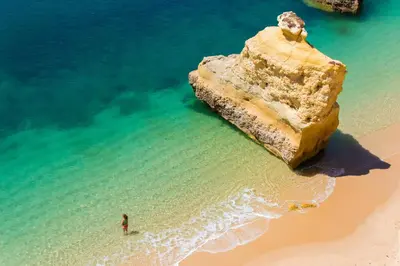 a person standing in the ocean next to a large rock at Cool Grey Albufeira in Albufeira