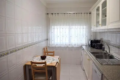 a white kitchen with a small table and a sink at Quarteira Comfortable Apartment in Quarteira