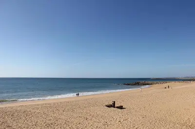 a beach with a bench in the sand and the ocean at Quarteira Comfortable Apartment in Quarteira