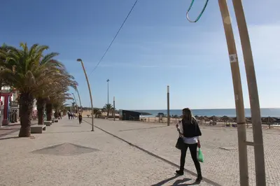 a woman walking down a sidewalk near the beach at Quarteira Comfortable Apartment in Quarteira