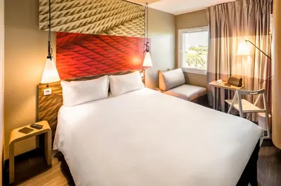a bedroom with a large white bed and a chair at Hotel ibis Faro Algarve in Faro