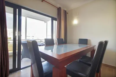 a dining room table with chairs and a large window at Apt 2 Quartos, BBQ, AC, Varanda, Prestige For Home in Quarteira