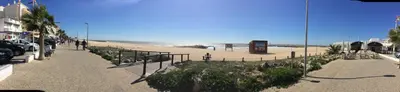 a sandy beach with people walking on the sidewalk at Apt 2 Quartos, BBQ, AC, Varanda, Prestige For Home in Quarteira