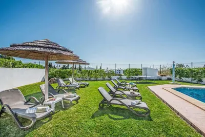 a row of lounge chairs and an umbrella next to a pool at Villa Damara in Albufeira