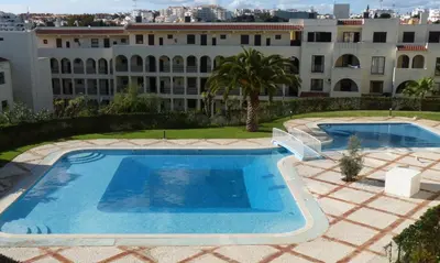 a pool with two chairs and a building at Apartamento bem localizado in Albufeira