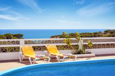 two chairs and a swimming pool with the ocean in the background at Villa Coelha in Albufeira