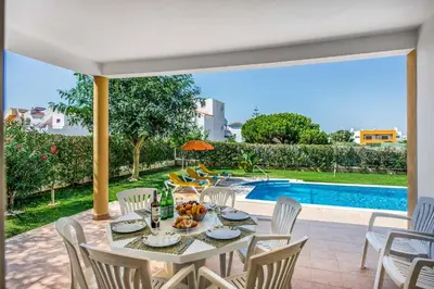 a dining table and chairs next to a swimming pool at Villa Altair in Albufeira